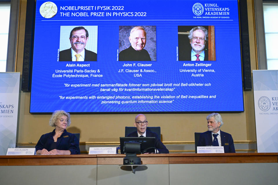 El secretario general de la Real Academia Sueca de Ciencias, Hans Ellegren, en el centro, y los miembros del Comité del Nobel para Física, Eva Olsson, a la izquierda, y Thors Hans Hansson, a la derecha, anuncian a los ganadores del Nobel de Física de 2022, de izquierda a derecha en la pantalla Alain Aspect, John F. Clauser y Anton Zeilinger, en una conferencia de prensa de la Academia en Estocolmo, Suecia, el martes 4 de octubre de 2022.. (Jonas Ekstromer /TT News Agency via AP)