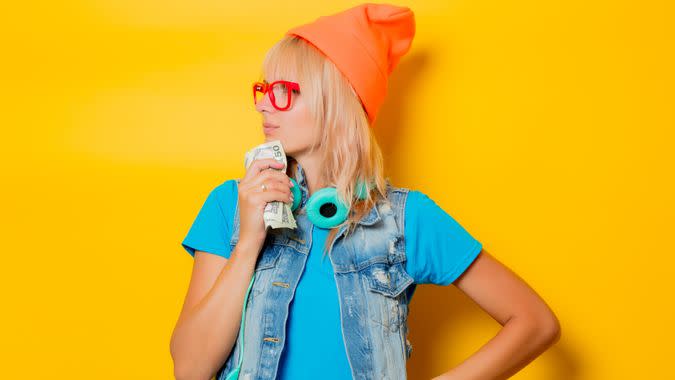 portrait of young trendy girl orange hat with money on yellow background.