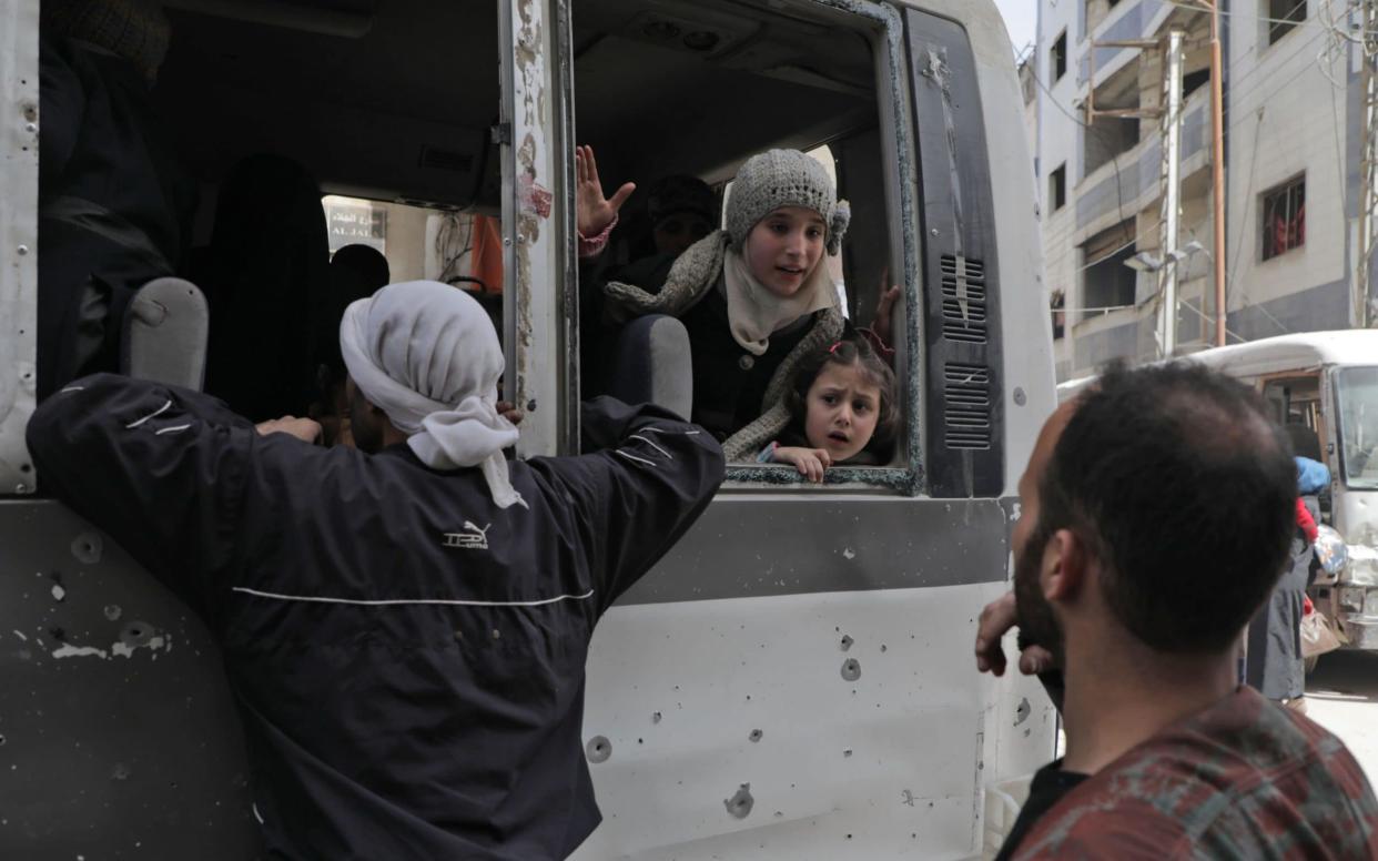 Syrian children speak to a man from out the window of a vehicle during a civilian evacuation by the Syrian Red Crescent in the rebel-held Eastern Ghouta enclave - AFP