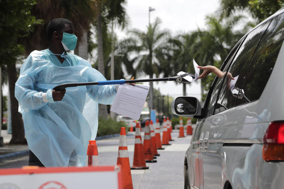 Healthcare worker Dante Hills, left, passes paperwork to a woman in a vehicle at a COVID-19 testing site outside of Marlins Park, Monday, July 27, 2020, in Miami. (Lynne Sladky/AP)