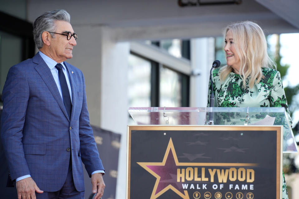 Eugene Levy and individual at a Hollywood Walk of Fame ceremony, standing by a podium with a star plaque