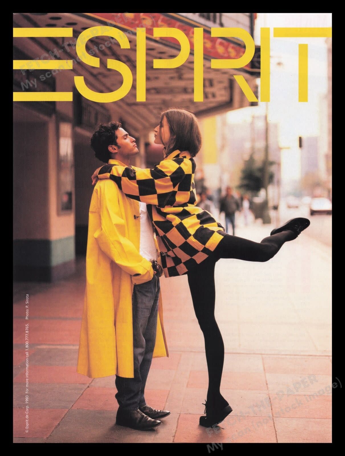 Esprit clothing 1993 print advertisement, woman is wearing a checkered yellow and black dress with focus on black tights, she has one leg up like a ballerina, while holding onto the shoulders of a man wearing a yellow trench coat, with city scene in the b