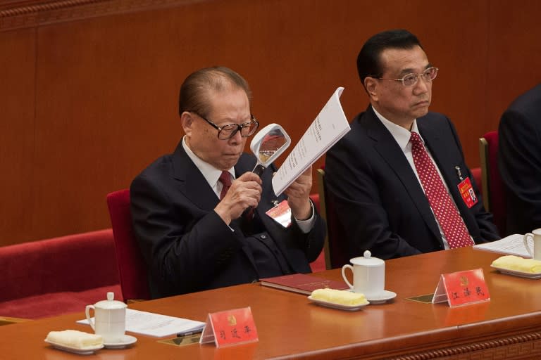 China's former president Jiang Zemin, sitting next to Premier Li Keqiang (R), reads papers with a magnifying glass as he listens to President Xi Jinping's address at the opening of the 19th Communist Party Congress