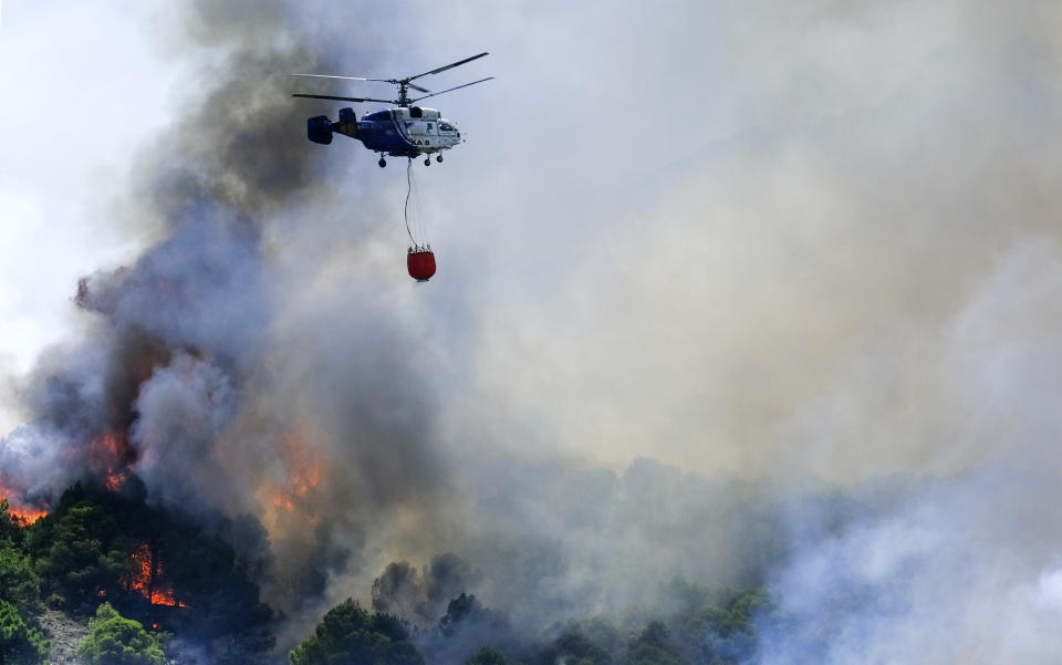 A helicopter launches water as a wildfire advances near a residential area in Alhaurin de la Torre, Malaga, Spain, Saturday, July 16, 2022. Wildfires continue to spread across Spain as firefighters work to bring them under control. (AP Photo/Gregorio Marrero)