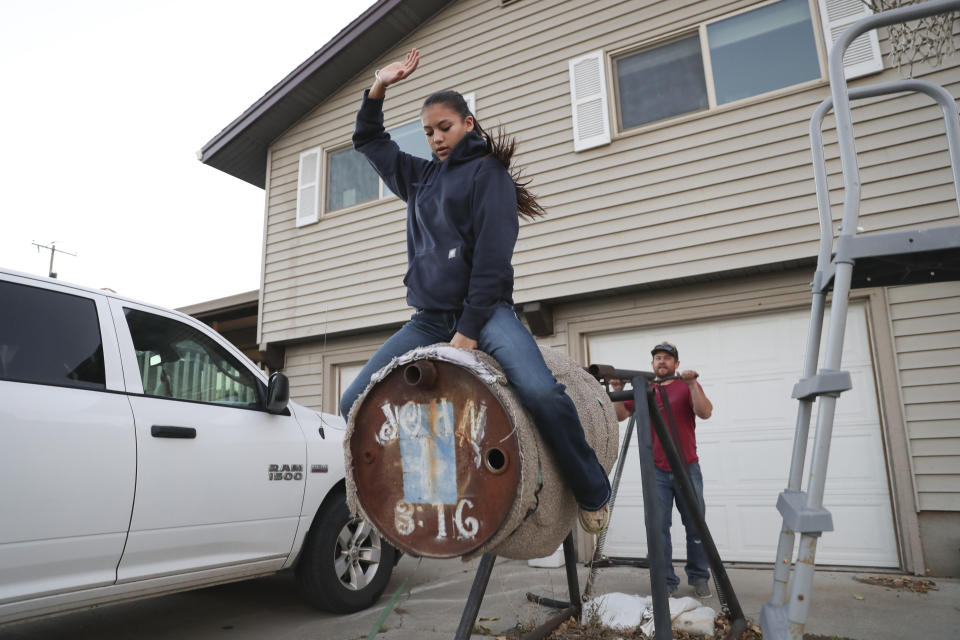 Najiah Knight uses a practice barrel to work on bull riding skills with the help of her father, Andrew, at the family's home in Arlington, Ore., Wednesday, Oct. 18, 2023. Najiah, a high school junior from small-town Oregon, is on a yearslong quest to become the first woman to compete at the top level of the Professional Bull Riders tour. (AP Photo/Amanda Loman)
