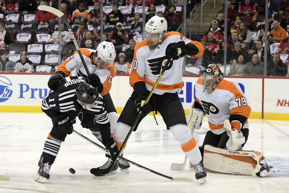 New Jersey Devils left wing Andreas Johnsson (11) vies for the puck against Philadelphia Flyers' Rasmus Ristolainen (70) and Travis Sanheim (6) as Flyers goaltender Carter Hart (79) watches during the first period of an NHL hockey game Wednesday, Dec. 8, 2021, in Newark, N.J. (AP Photo/Bill Kostroun)