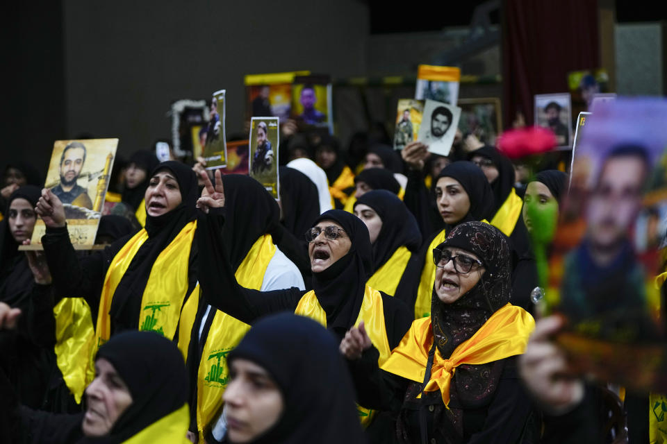 Supporters of the Iranian-backed Hezbollah group hold pictures of their relatives who died fighting with Hezbollah as raise their fists in salute while listen to a speech by Hezbollah leader Sayyed Hassan Nasrallah via a video link, during a ceremony marking the "Hezbollah Martyr Day," in the southern Beirut suburb of Dahiyeh, Lebanon, Saturday, Nov. 11, 2023. (AP Photo/Hassan Ammar)