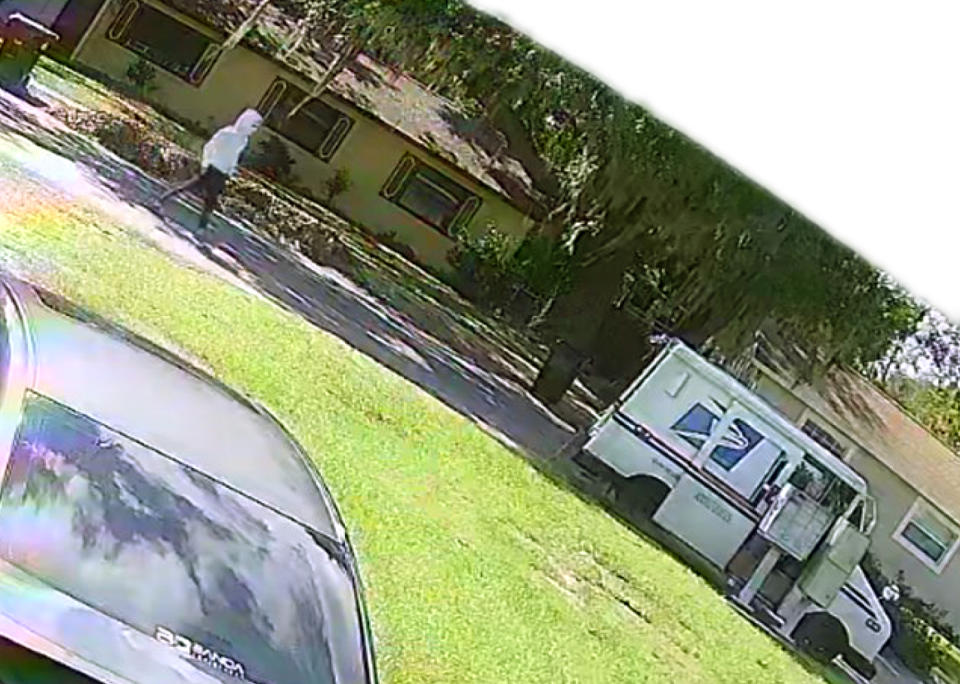 An October 2022 surveillance photo of an armed robber approaching a mail carrier. <cite>The Conversation via <a href="https://www.documentcloud.org/documents/23809211-usa_v_capers__flmdce-23-01027__00010" rel="nofollow noopener" target="_blank" data-ylk="slk:court records;elm:context_link;itc:0;sec:content-canvas" class="link ">court records</a></cite>