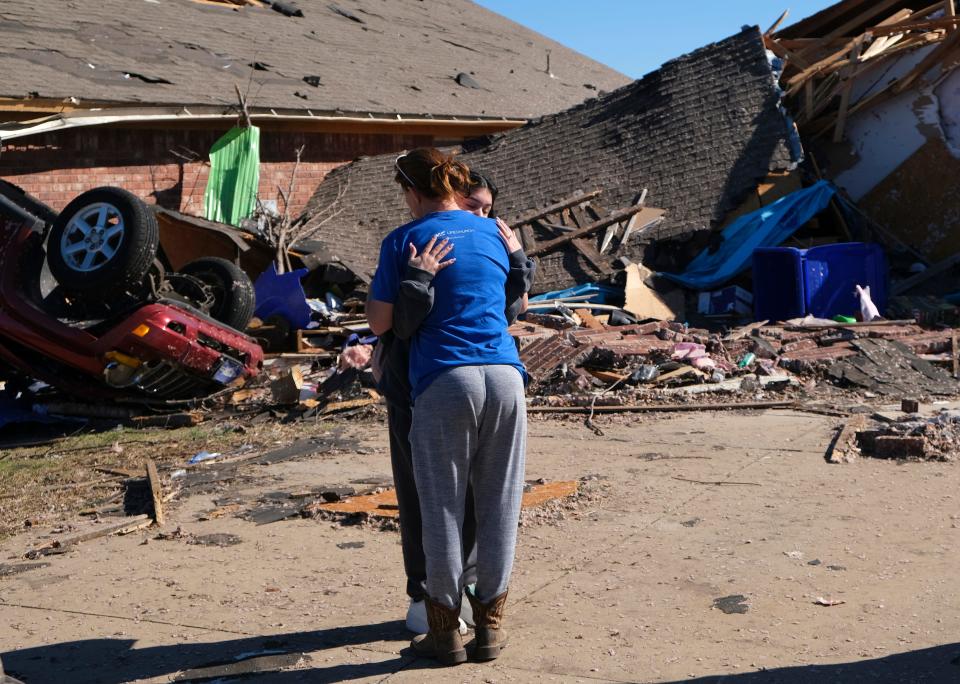 Adriana Sanders gets a hug in front of her house and car Monday. Sanders rode out a Sunday tornado in Norman with others in a middle bathroom.
