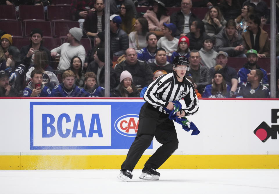 Linesman Trent Knorr picks up a Vancouver Canucks jersey that was thrown onto the ice by a fan as Vancouver and the Winnipeg Jets play during the third period of an NHL hockey game, Saturday, Dec. 17, 2022 in Vancouver, British Columbia. (Darryl Dyck/The Canadian Press via AP)