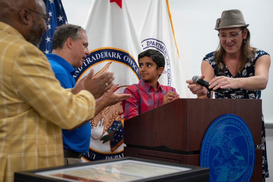 Eighth grader Mihir Shah, 12, center, is cheered on by James Wilson, USPTO assistant regional director, left, and robotics mentors Dan Champoux and Autumn Mahoney after delivering a speech while being honored with other student inventors from the Bloomfield Hills school district's GEKOT FIRST LEGO League Robotics Team for a patent of their e-scooter safety device at River Place in Detroit on Tuesday, Aug. 9, 2023.