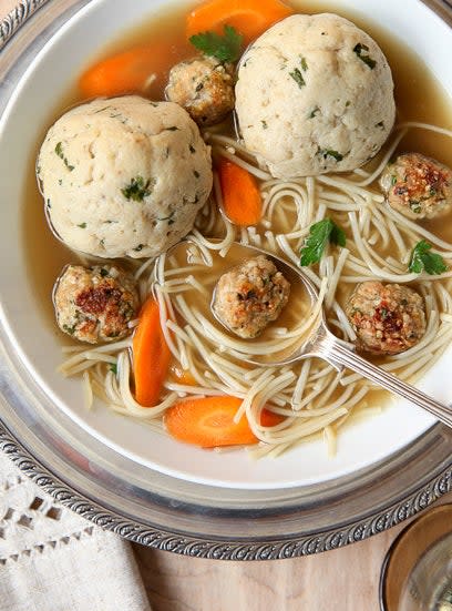 A bowl of soup with thin, long noodles, chicken meatballs, matzo balls, and carrots in chicken broth.