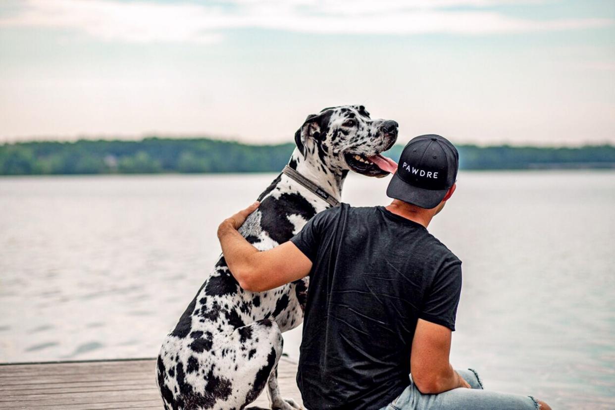 man with his dog on a dock and wearing a hat with the word "Pawdre" on the front