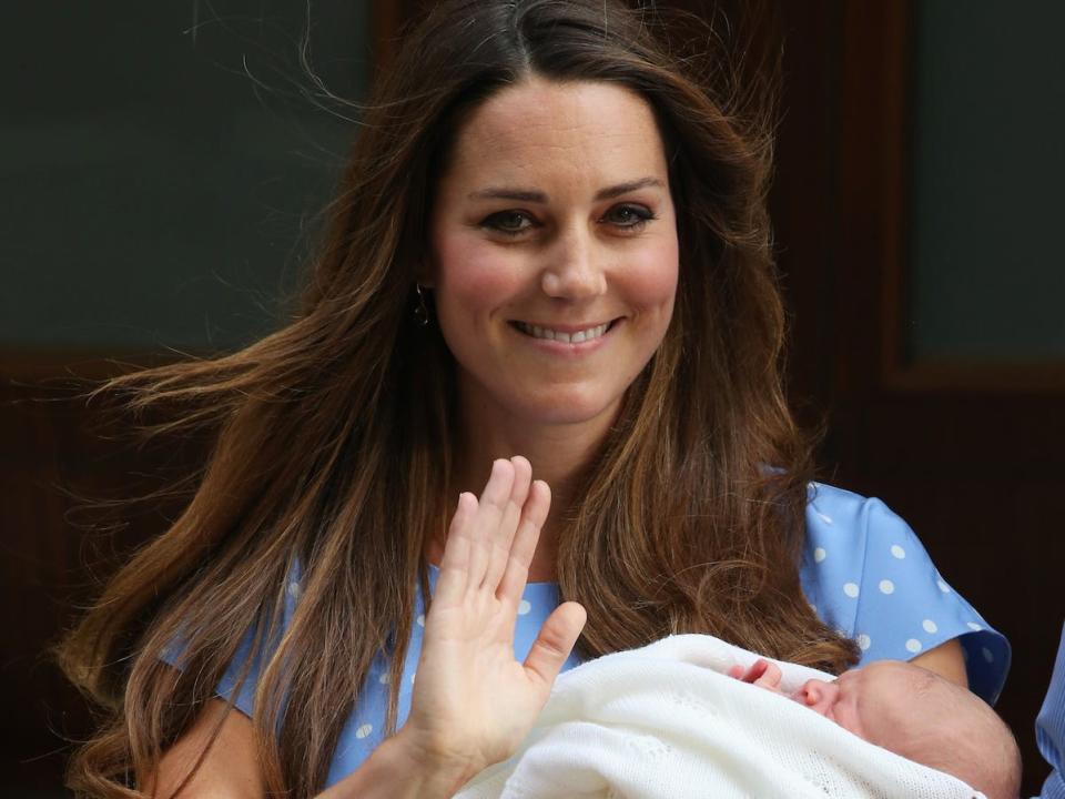Kate Middleton waves to photographers after giving birth to Prince George. She holds Prince George in a blanket.