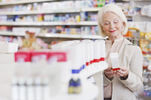 A senior woman holds an item she picked up off a shelf in a pharmacy store.