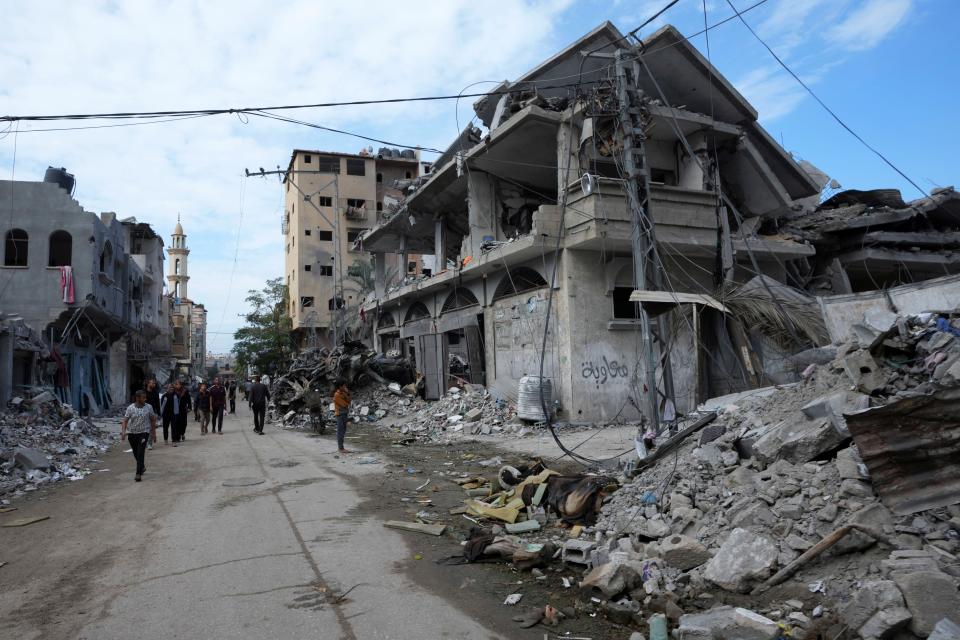 Palestinians walk past the buildings destroyed in the Israeli bombardment of the Gaza Strip, at the main road in Bureij refugee camp, Gaza Strip, Tuesday, Nov. 14, 2023. (AP Photo/Adel Hana)