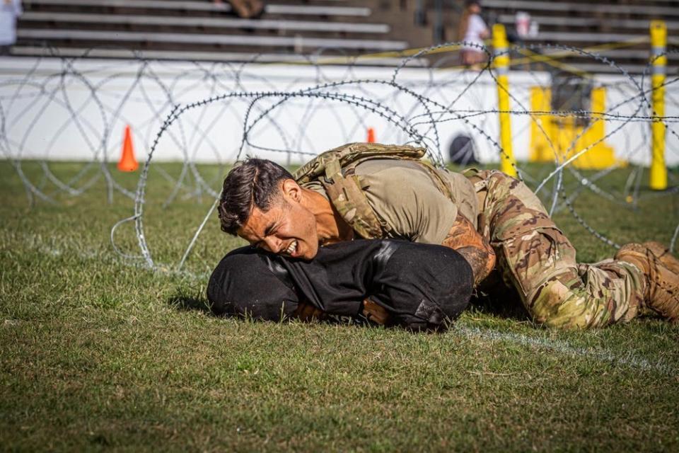 A US Army soldier has a pained expression as he carries a black sack while maneuvering on the ground.