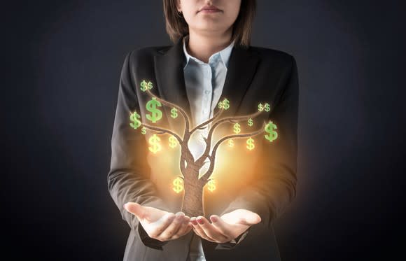 A businesswoman with hands outstretched and holding a graphic of a tree with green dollar signs hanging from it.