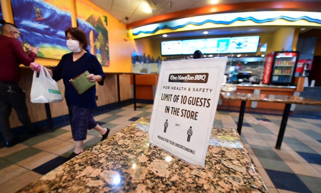 A customer walks away with takeout at a fast-food restaurant limiting only 10 guests with chairs cleared off the floor in Alhambra, California on July 1, 2020. New regulations in some counties for certain businesses have come into effect again as coronavirus cases hit record highs.