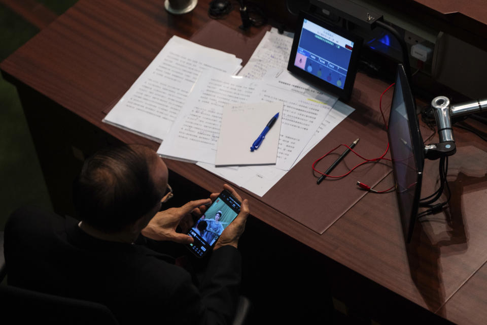 A lawmaker watches his phone during the second reading of the Basic Law Article 23 legislation at the Legislative Council in Hong Kong, Tuesday, March 19, 2024. (AP Photo/Louise Delmotte)