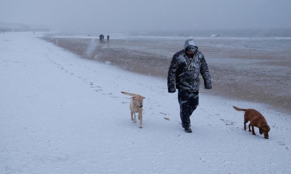 A dog walker leaves footprints in the snow on Whitley Bay beach