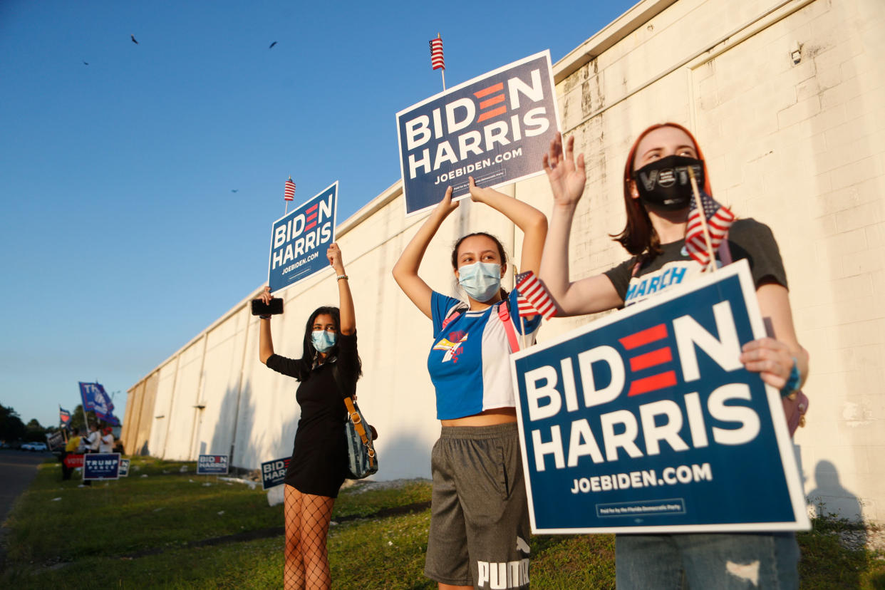 Three young women wave their Biden-Harris signs at the Town 'N Country Regional Public Library