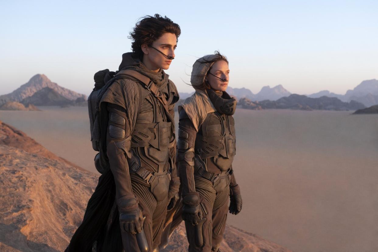 A man and a woman stand on the desert-like surface of an alien planet.