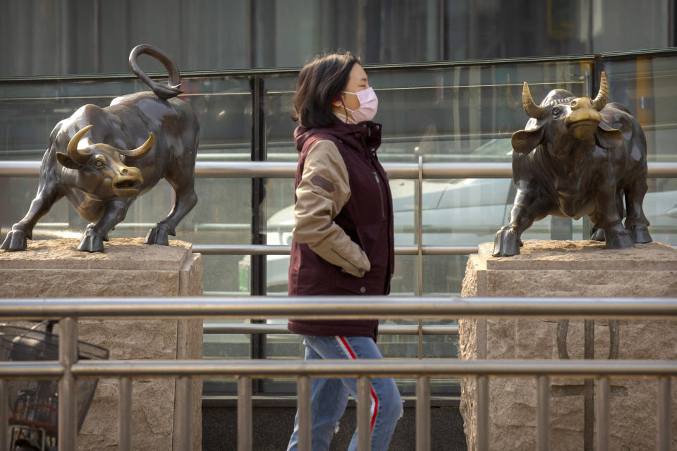 A woman wearing a face mask walks past statues of bulls in Beijing, Friday, Feb. 28, 2020. Asian stock markets fell further Friday on spreading virus fears, deepening an global rout after Wall Street endured its biggest one-day drop in nine years. (AP Photo/Mark Schiefelbein)