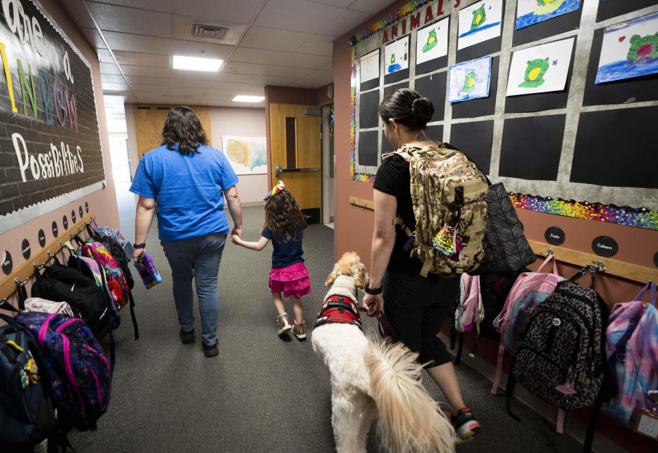 Vivien Henshall, a long-term substitute special education teacher, walks with Scarlett Rasmussen as Scarlett's mother, Chelsea, follows with service dog Riptide, at Parkside Elementary School Wednesday, May 17, 2023, in Grants Pass, Ore. Chelsea has fought for more than a year for her 8-year-old daughter, Scarlett, to attend full days at Parkside. (AP Photo/Lindsey Wasson)