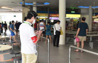 A safe-distancing enforcement officer wearing a red armband checks his phone at a food court in Singapore on Saturday, April 18, 2020. The officers have been deployed throughout the Southeast Asian city-state to ensure people maintain distance from one another as it grapples with a spike in coronavirus cases. (AP Photo/YK Chan)