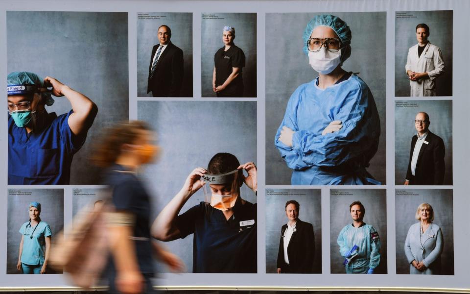 A woman wearing a face mask walks past an outdoor photography exhibition on healthcare workers in Melbourne - JAMES ROSS/EPA-EFE/Shutterstock