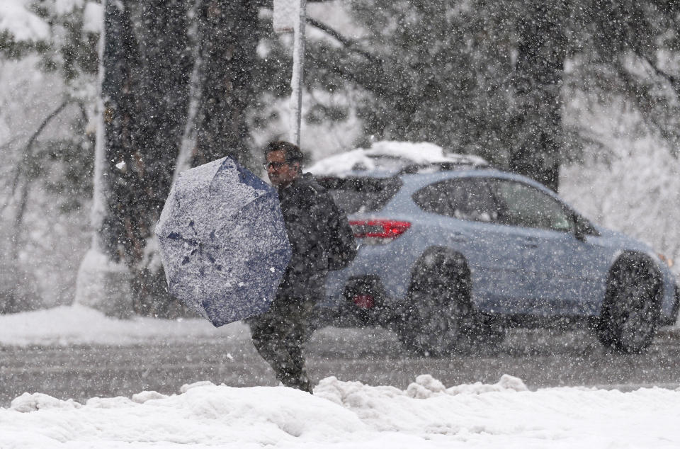 A pedestrian cleans off his umbrella while waiting for a bus at a stop along eastbound Speer Boulevard during a snow stormon Thursday, March 14, 2024, in Denver. Forecasters predict that the storm will persist until early Friday, snarling traffic along Colorado's Front Range communities. (AP Photo/David Zalubowski)