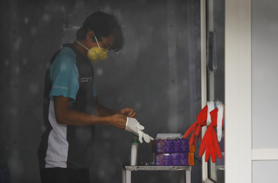 Nhuja Kaiju, of the RNA-16 volunteer group, takes off his gloves after assisting nurses at a hospital in Bhaktapur, Nepal, Tuesday, May 26, 2020. RNA-16 stands for “Rescue and Awareness” and the 16 kinds of disasters they have prepared to deal with, from Nepal’s devastating 2015 earthquake to road accidents. But the unique services of this group of three men and a woman in signature blue vests in the epidemic amount to a much greater sacrifice, said doctors, hospital officials and civic leaders. (AP Photo/Niranjan Shrestha)