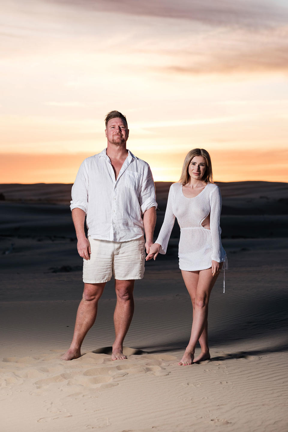Dean Wells and Aimee Woolley posing on a beach in front of a sunset