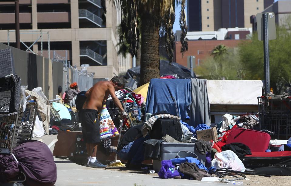 FILE - A man sweeps the sidewalk as tents and crude lean-tos crowd the sidewalks where many homeless people live along the streets on March 24, 2020, in Phoenix. The city is wrangling with two dueling lawsuits as it tries to manage a homelessness crisis that has converted its downtown into a tent city housing hundreds of people under the blazing desert sun just as summer temperatures soar into the 90s. (AP Photo/Ross D. Franklin, File)