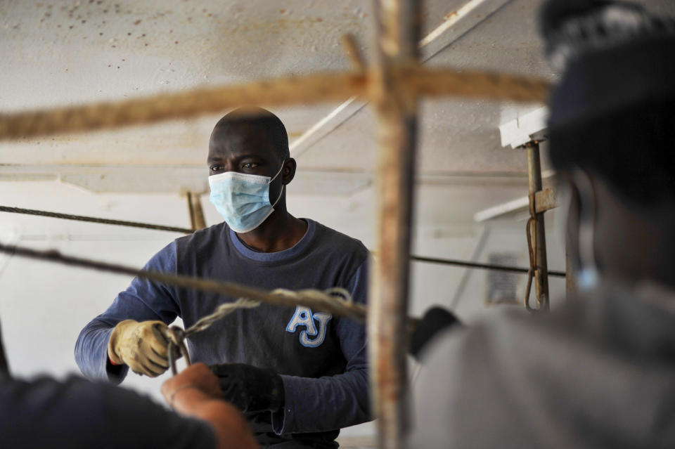 Ibrahima Mbaye, 41, from Senegal, fixes nets on the "Vincenzo Padre" fishing boat where he works as a fisherman, in the Island of Lampedusa, southern Italy, Thursday, May 13, 2021. The tiny island of Lampedusa, which is closer to Africa than the Italian mainland, is in the throes of yet another season of migrant arrivals, and Mbaye and his fellow countryman Waly Sarr can only watch from shore as their fellow African countrymen risk their lives to get here via smugglers' boats. (AP Photo/Salvatore Cavalli)