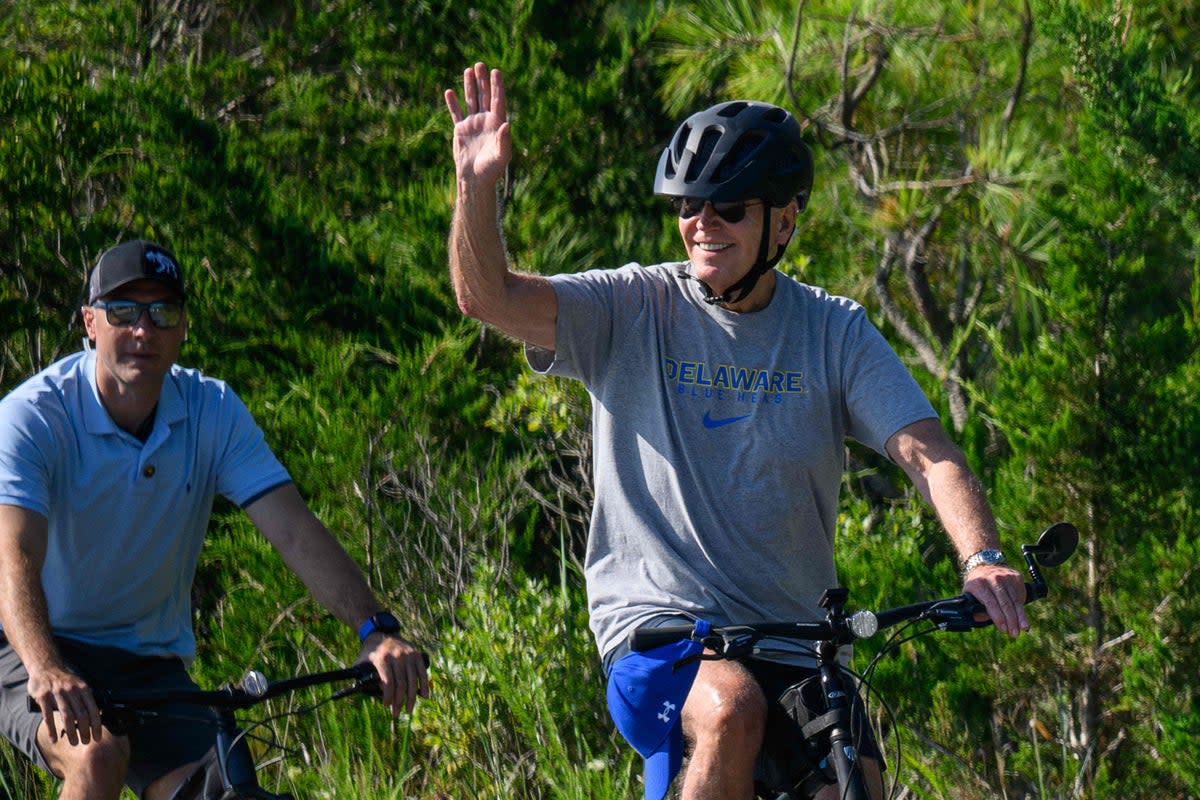 Joe Biden waves as he rides his bicycle through Cape Henlopen State Park in Rehoboth Beach on 13 August (AFP via Getty Images)