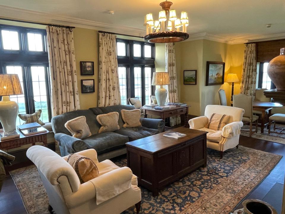 Living room with white chairs, a wooden chest, a blue couch, several lamps, and windows with curtains