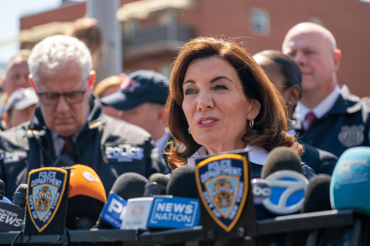 New York Gov. Kathy Hochul, with police officials behind her, speaks into a row of microphones.