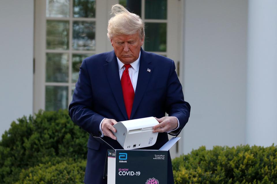 President Donald Trump opens a box containing a 5-minute test for COVID-19 from Abbott Laboratories as Stephen Hahn, commissioner of the U.S. Food and Drug Administration, speaks about the coronavirus in the Rose Garden of the White House, Monday, March 30, 2020, in Washington.