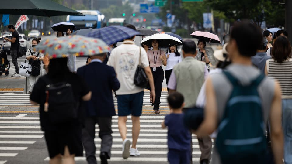 Pedestrians holding umbrellas cross a street in Seoul, South Korea, on Monday, Aug. 5, 2024. South Korea's fertility rate is the lowest in the world, at 0.72 children per woman in 2023. - SeongJoon Cho/Bloomberg/Getty Images