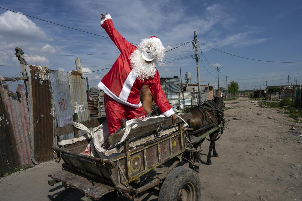 Tito Perez, dressed as Santa Claus, waves to children while standing on the back of a horse cart, at a pre-Christmas celebration organized by "Los Chicos de la Via" soup kitchen, in Buenos Aires, Argentina, Dec. 23, 2023. (AP Photo/Rodrigo Abd)