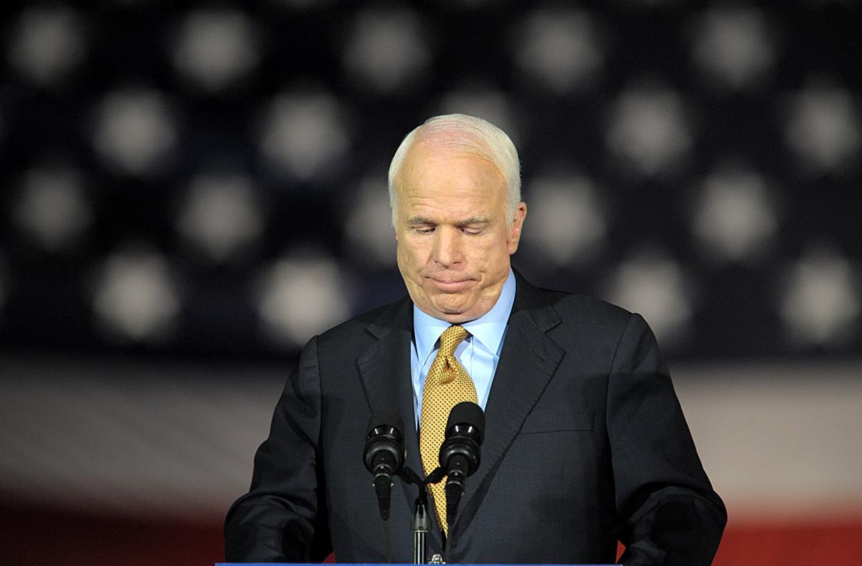 John McCain looks down while standing at a podium