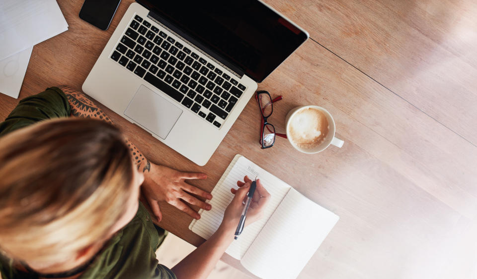 Top view shot of woman sitting at table with laptop and coffee writing on notebook. Female making to do list on diary.