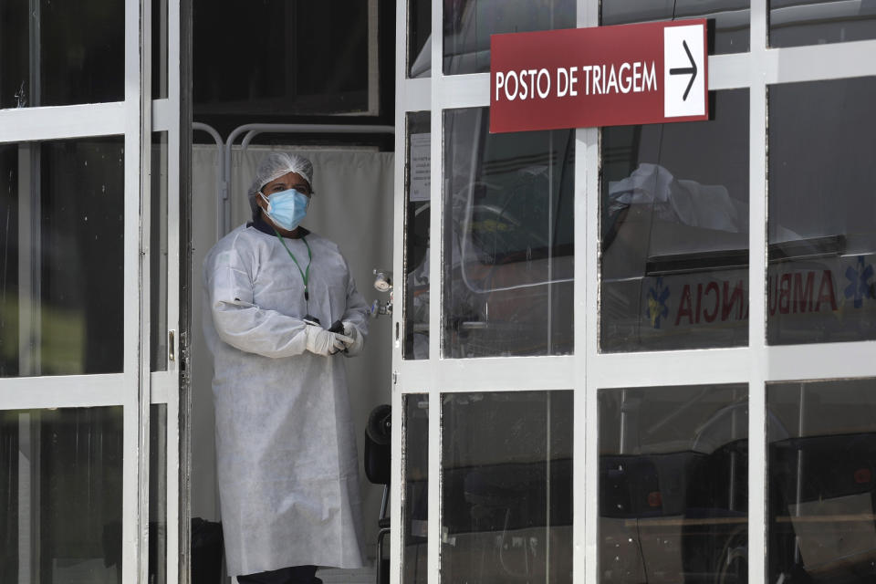 A health worker stands at the entrance of the HRAN Hospital that specializes in the care of new coronavirus cases, after a new patient arrived in Brasilia, Brazil, Thursday, Jan. 7, 2021. (AP Photo/Eraldo Peres)