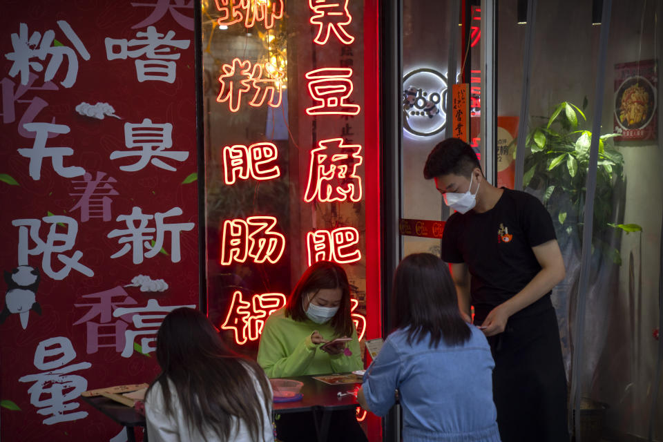 A woman wearing a face mask orders food at a sidewalk restaurant at a shopping and office complex in Beijing, Wednesday, Aug. 24, 2022. China is easing its tight restrictions on visas after it largely suspended issuing them to students and others more than two years ago at the start of the COVID-19 pandemic. (AP Photo/Mark Schiefelbein)