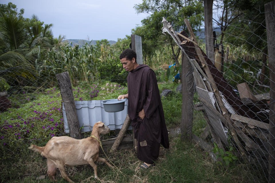 Seminarian Alfredo Santos, 21, brings water to a goat at the drug rehabilitation center in Mission San Francisco de Asis, Honduras, Tuesday, June 29, 2021. A year ago, Brother Santos, who used to go out to pray on the road, was kidnapped, beaten, doused with gasoline and subjected to a simulated hanging. He still is not able to talk about it. (AP Photo/Rodrigo Abd)