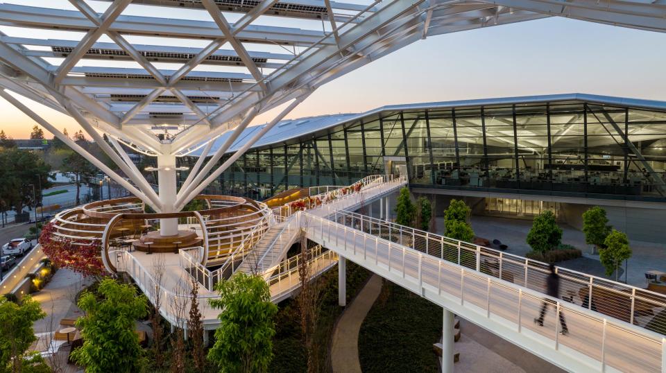 A walk way between Nvidia's buildings at its headquarters with some trees around it and a white metallic structure above the walkway