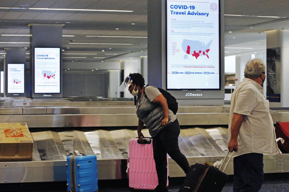 An arriving passenger wearing a face shield, left, collects her luggage in the baggage claim area of LaGuardia Airport's Terminal B, Thursday, June 25, 2020, in New York. New York, Connecticut and New Jersey are asking visitors from states with high coronavirus infection rates to quarantine for 14 days. The "travel advisory" affects three adjacent Northeastern states that managed to check the spread of the virus this spring as New York City became a hot spot. Travelers from mostly southern and southwestern states including Florida, Texas Arizona and Utah will be affected starting Thursday. The two-week quarantine will last two weeks from the time of last contact within the identified state. (AP Photo/Kathy Willens)