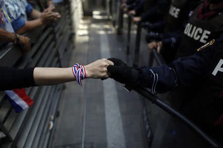 An anti-government protester holds hands with an anti-riot police officer across the closed gates outside the headquarters of the ruling Puea Thai Party of Prime Minister Yingluck Shinawatra in Bangkok in this November 29, 2013 file photo. THAILAND-POLITICS/ REUTERS/Damir Sagolj/Files